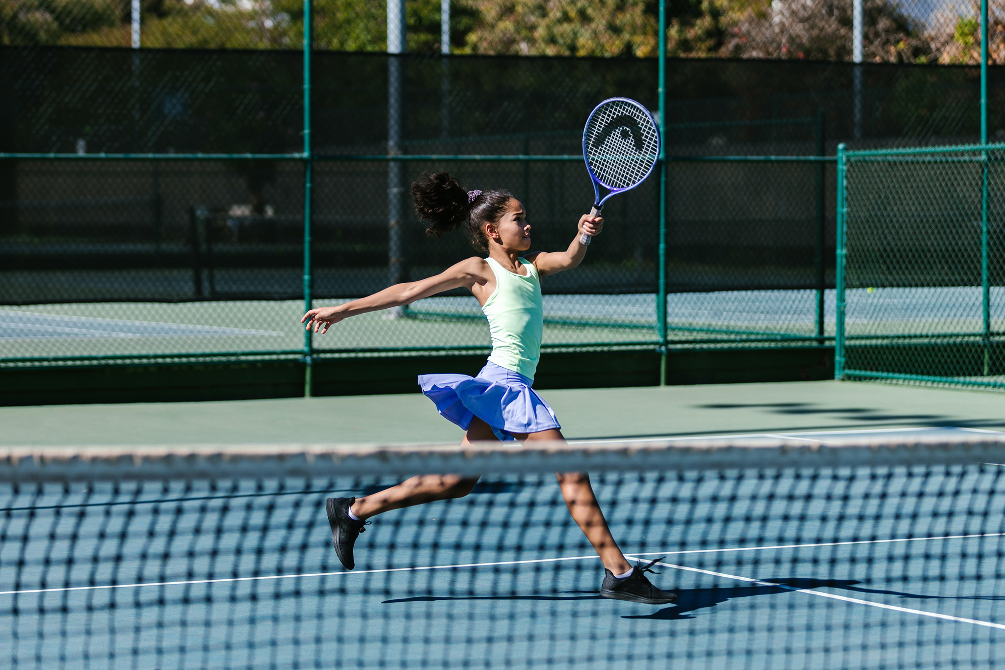 An action photo of a young girl swinging a tennis racket